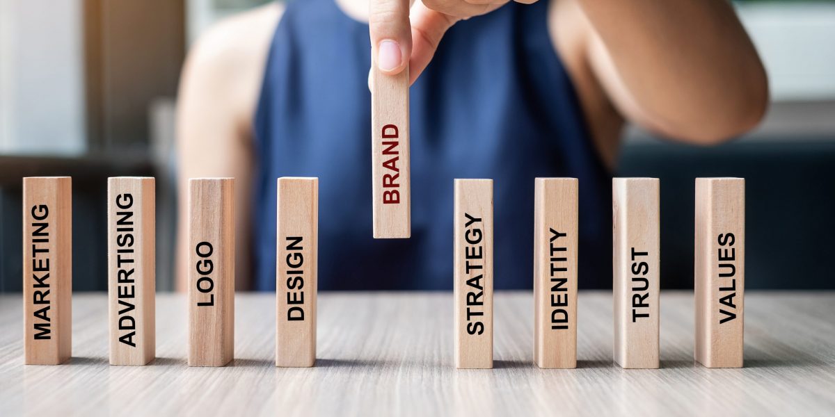 Businesswoman hand placing or pulling wooden Dominoes with BRAND text. and Marketing, Advertising, Logo, Design, Strategy, Identity, Trust and Values. Product development concept